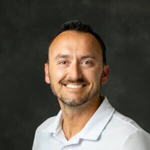 A man with a beard is smiling for the camera while wearing a white shirt.