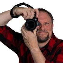 A man in a plaid shirt is taking a picture with a camera.