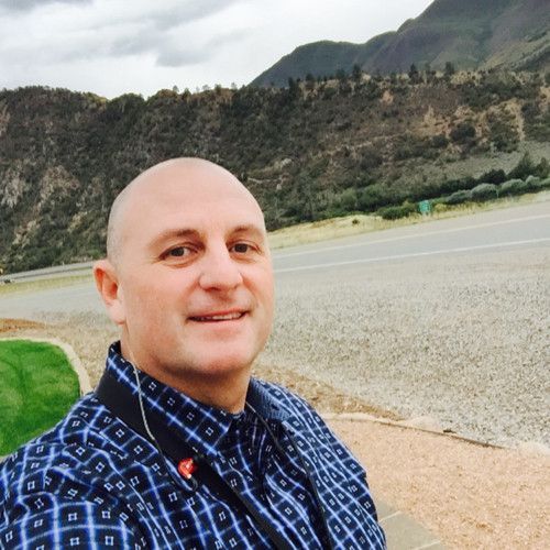 A man is taking a selfie with a bridge in the background.
