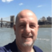 A man is taking a selfie with a bridge in the background.