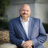 A bald man with a beard is wearing a blue suit and white shirt.