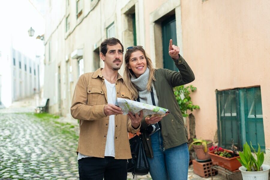 A man and a woman are standing on a cobblestone street looking at a map.