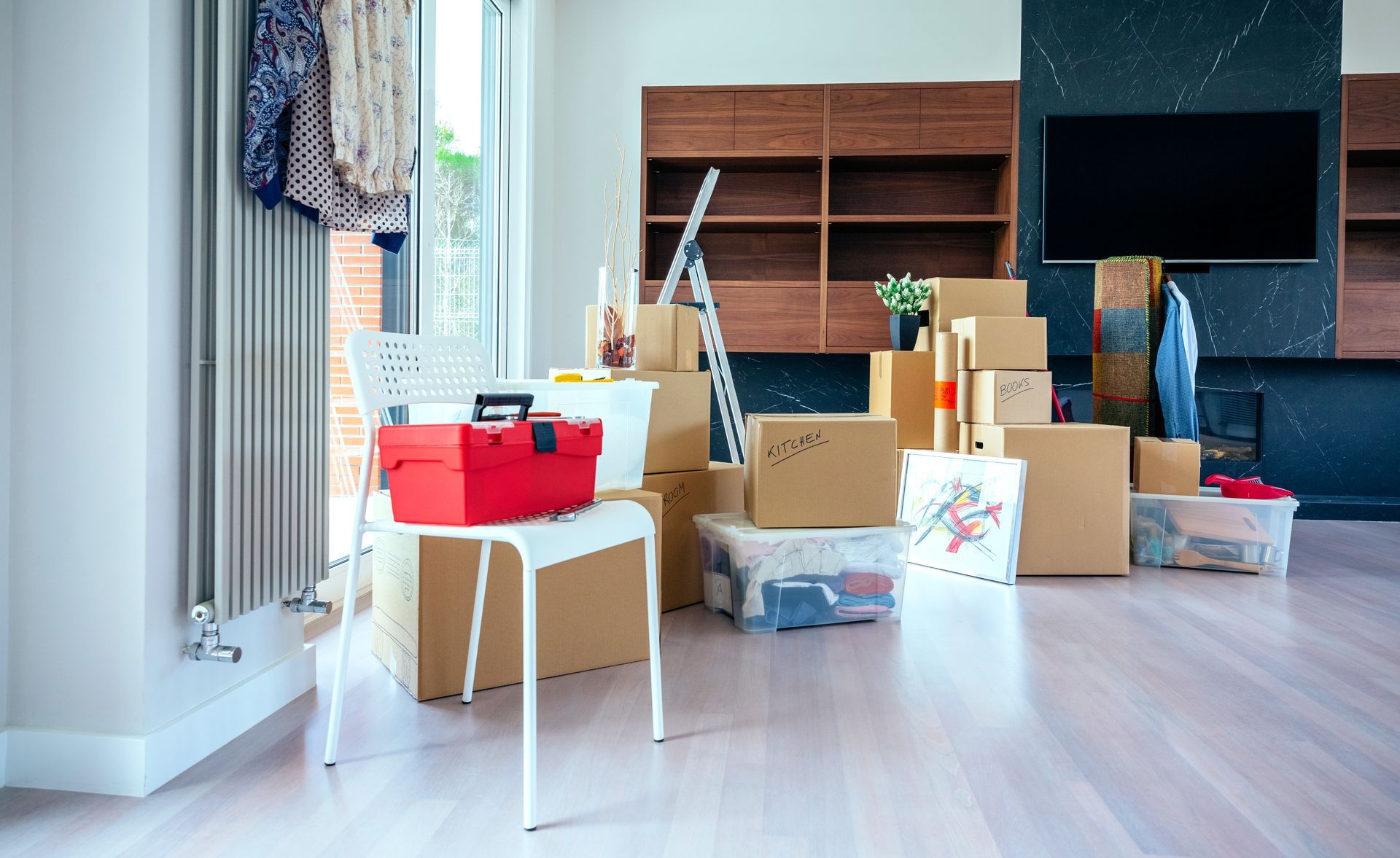 Boxes and belongings in a room, ready for moving. A toolbox sits on a chair.