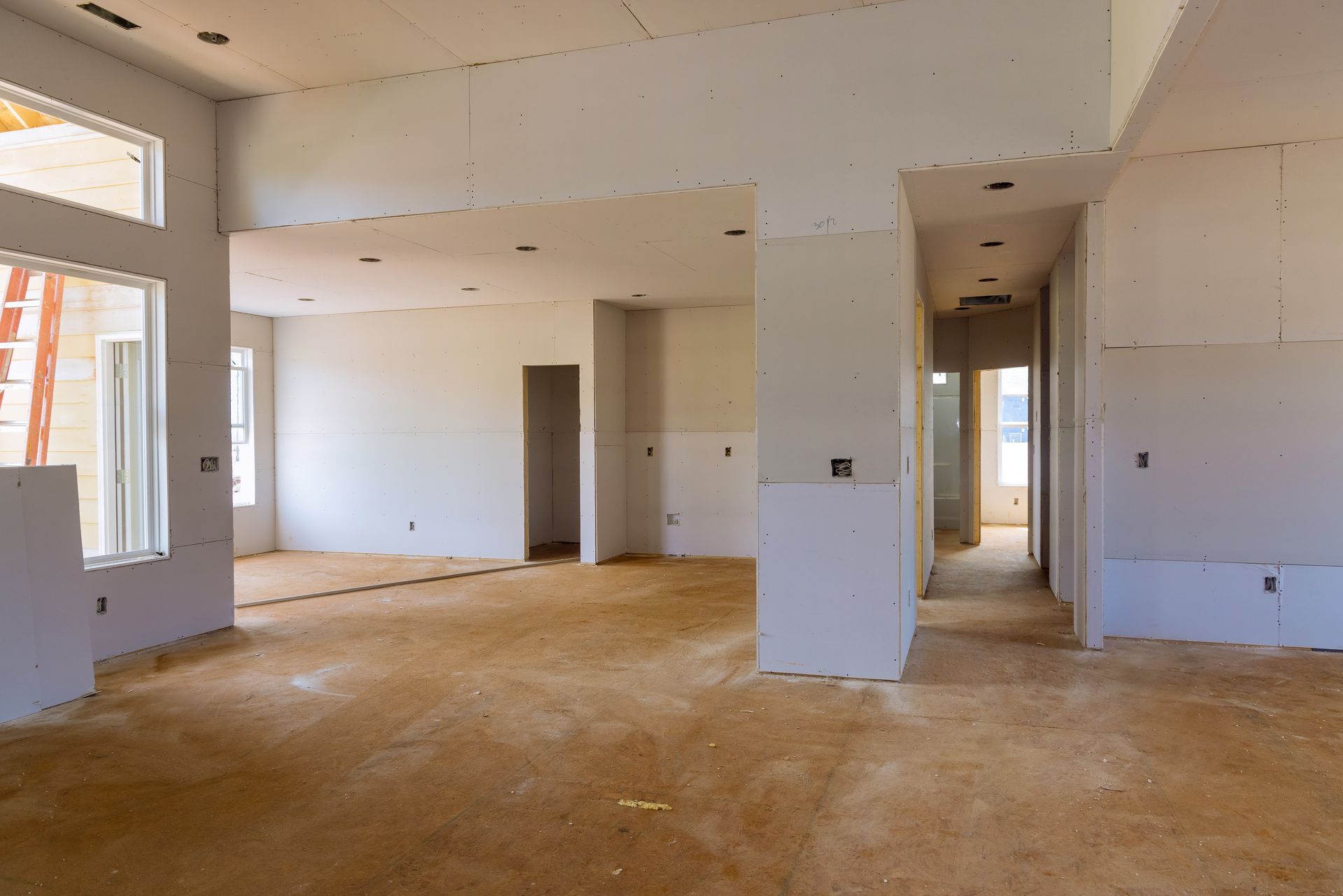 Interior of a house under construction; drywall walls, unfinished floors, doorways, windows, and exposed electrical boxes.
