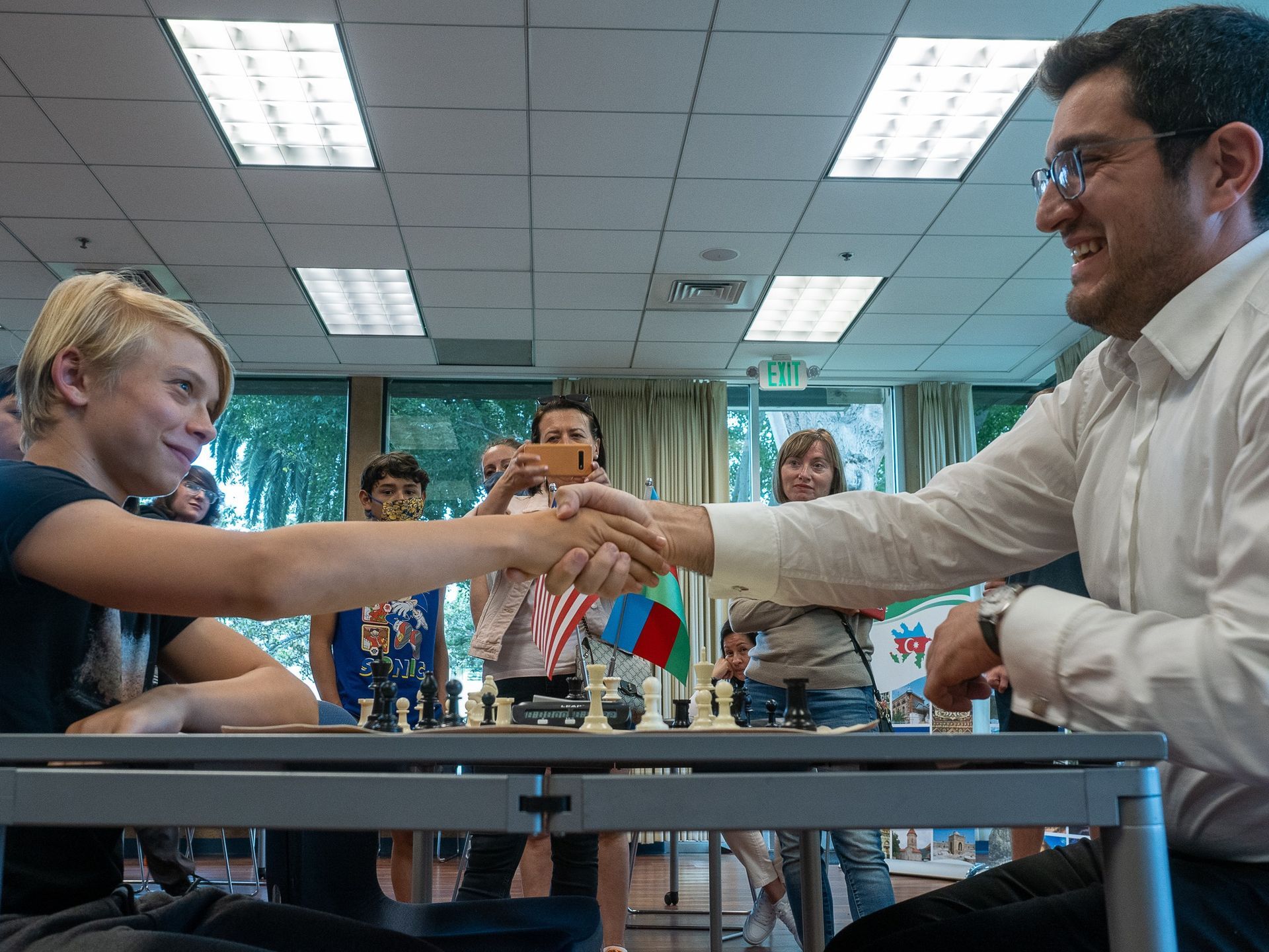 A man and a boy are shaking hands in front of a chess board.