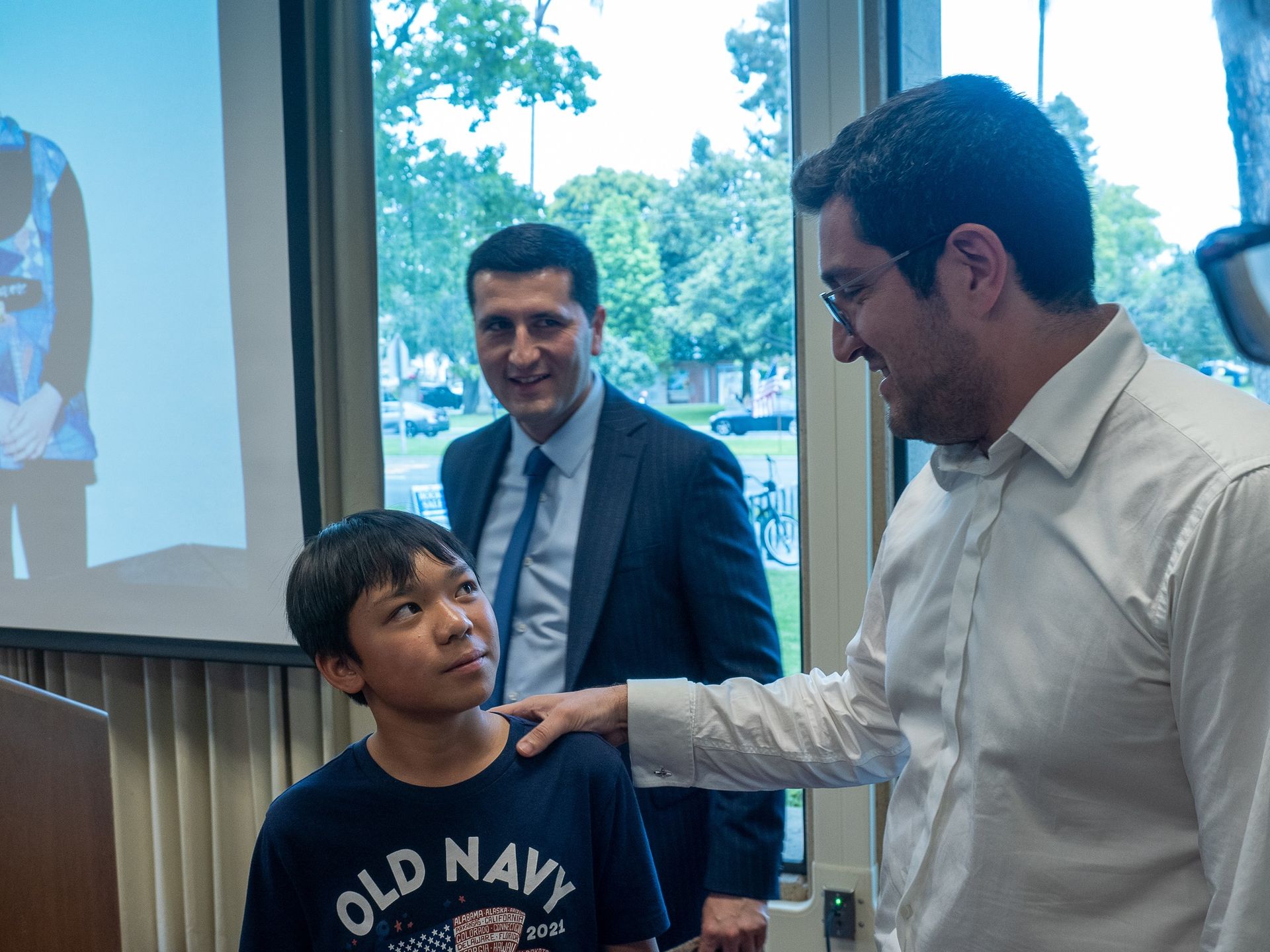 Two men are talking to a young boy wearing an old navy shirt