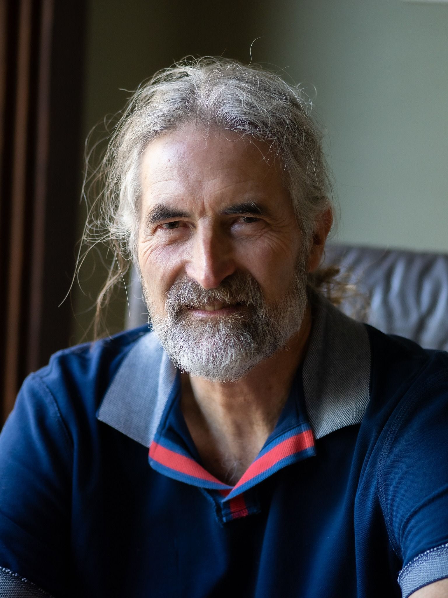 A man with long hair and a beard is sitting on a couch.