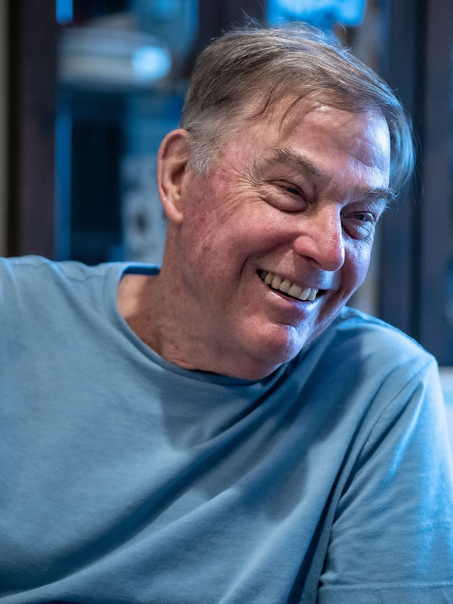 A man in a blue shirt is smiling with his eyes closed.