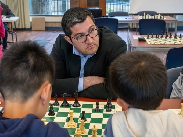 A man is playing chess with two young boys