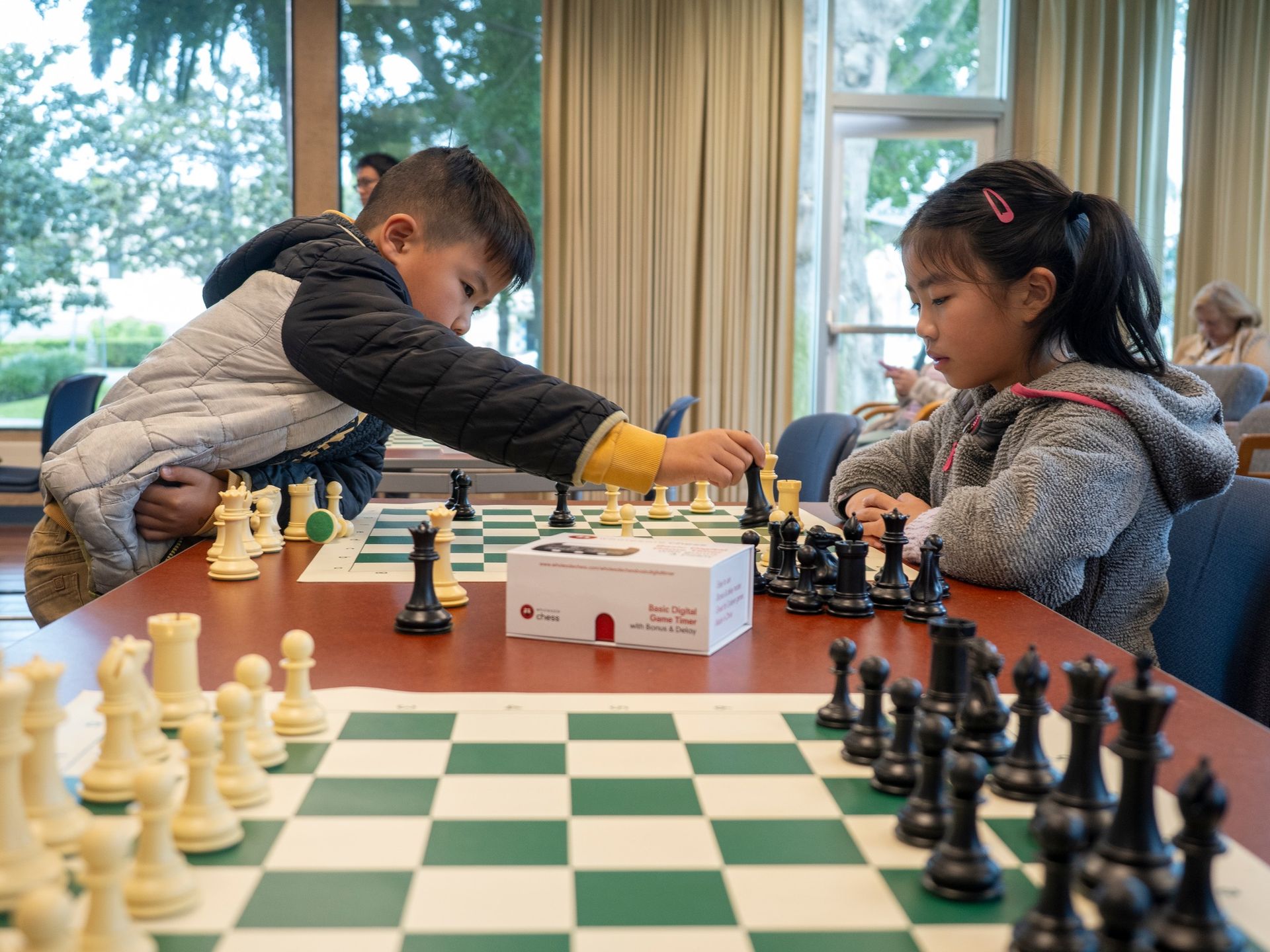 A boy and a girl are playing chess at a table.