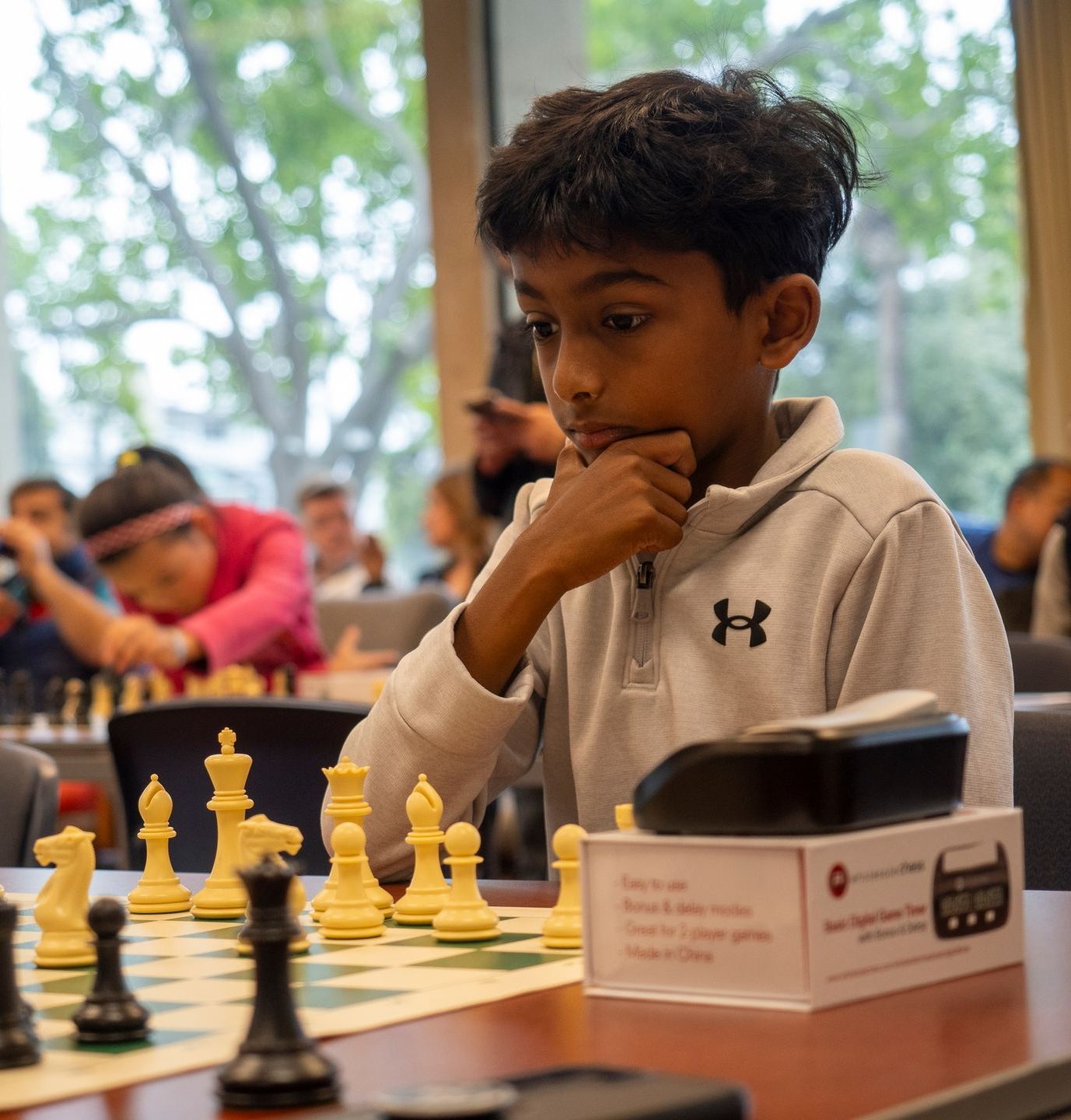 A young boy wearing an under armour shirt is playing chess