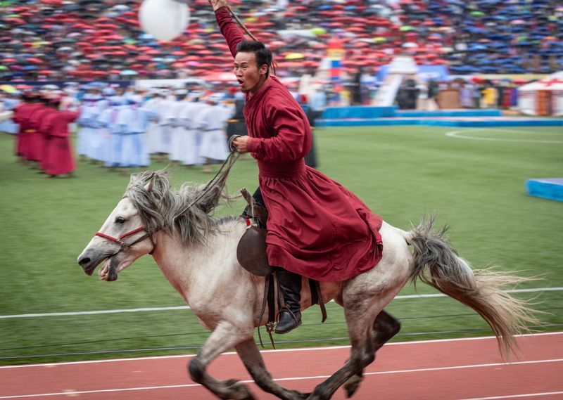 A man in a red robe is riding a white horse on a track.