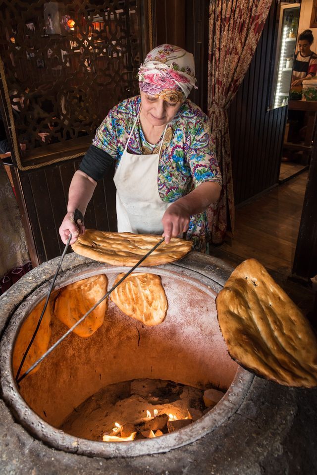 A woman is cooking bread in a tandoor oven.