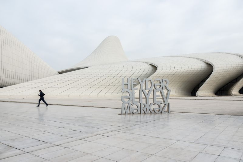 A man is walking in front of a building that says heydar sliyev