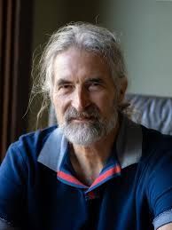 A man with long hair and a beard is sitting on a couch.