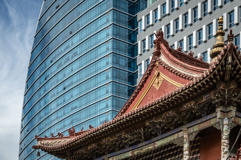 A chinese building with a red roof in front of a tall building.