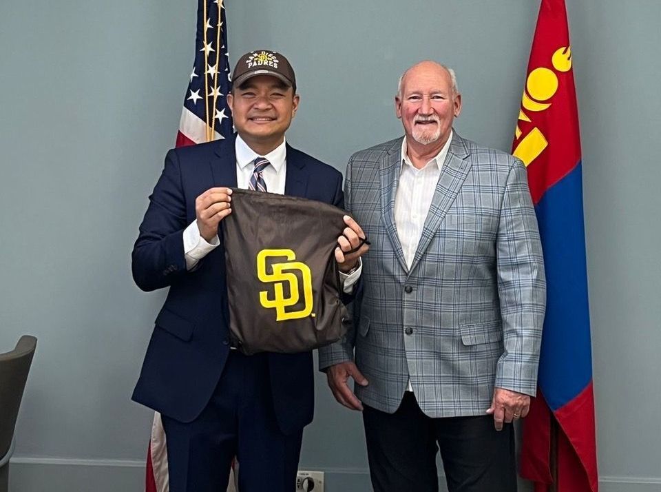 Two men are standing next to each other holding a bag with a san diego padres logo on it.