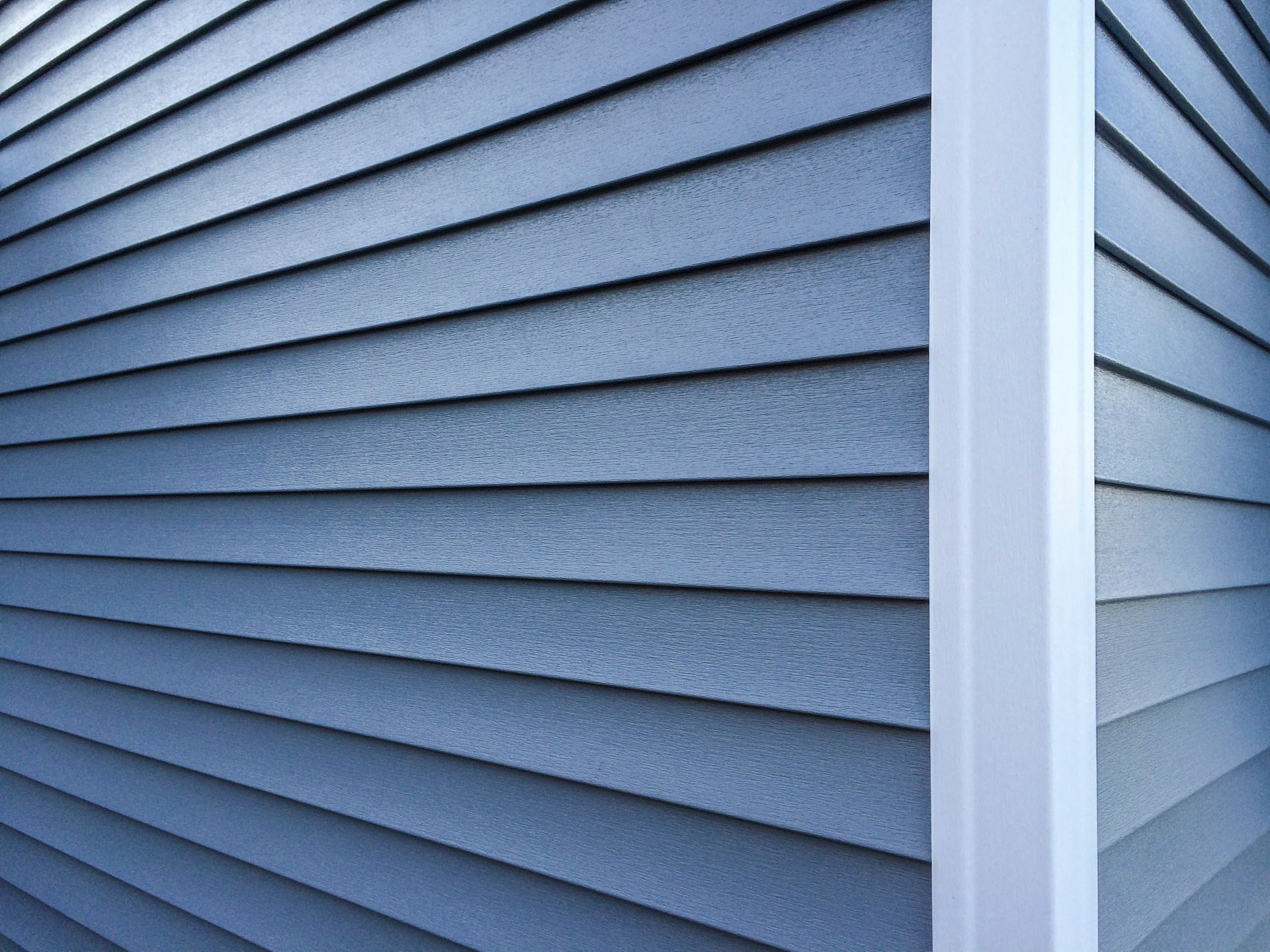 Blue vinyl siding corner with white trim on a house exterior