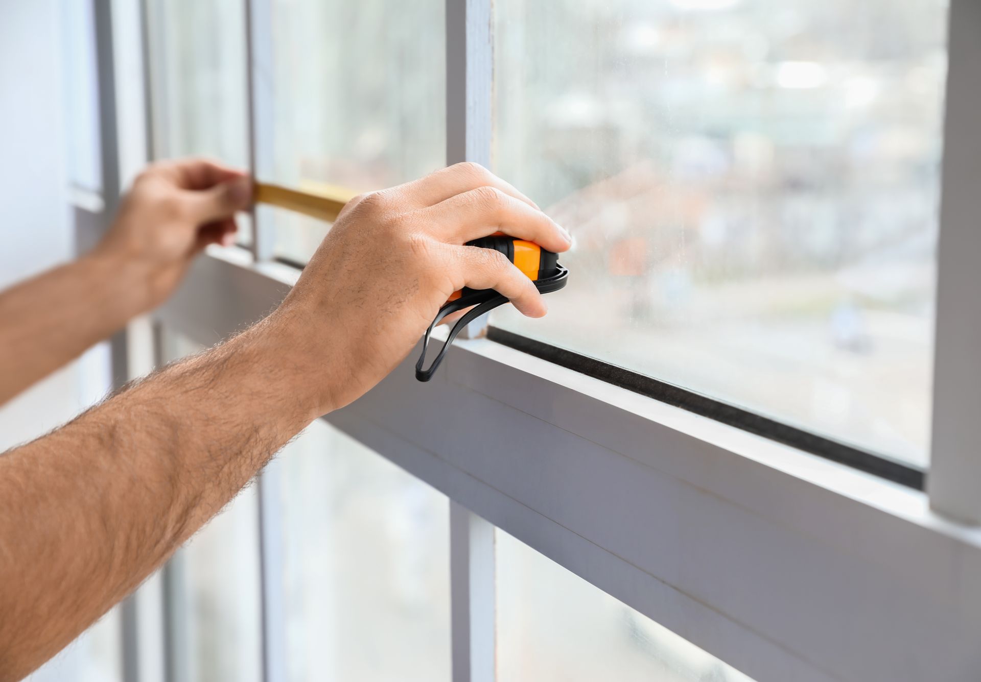 Hands opening a white window latch on a glass window frame