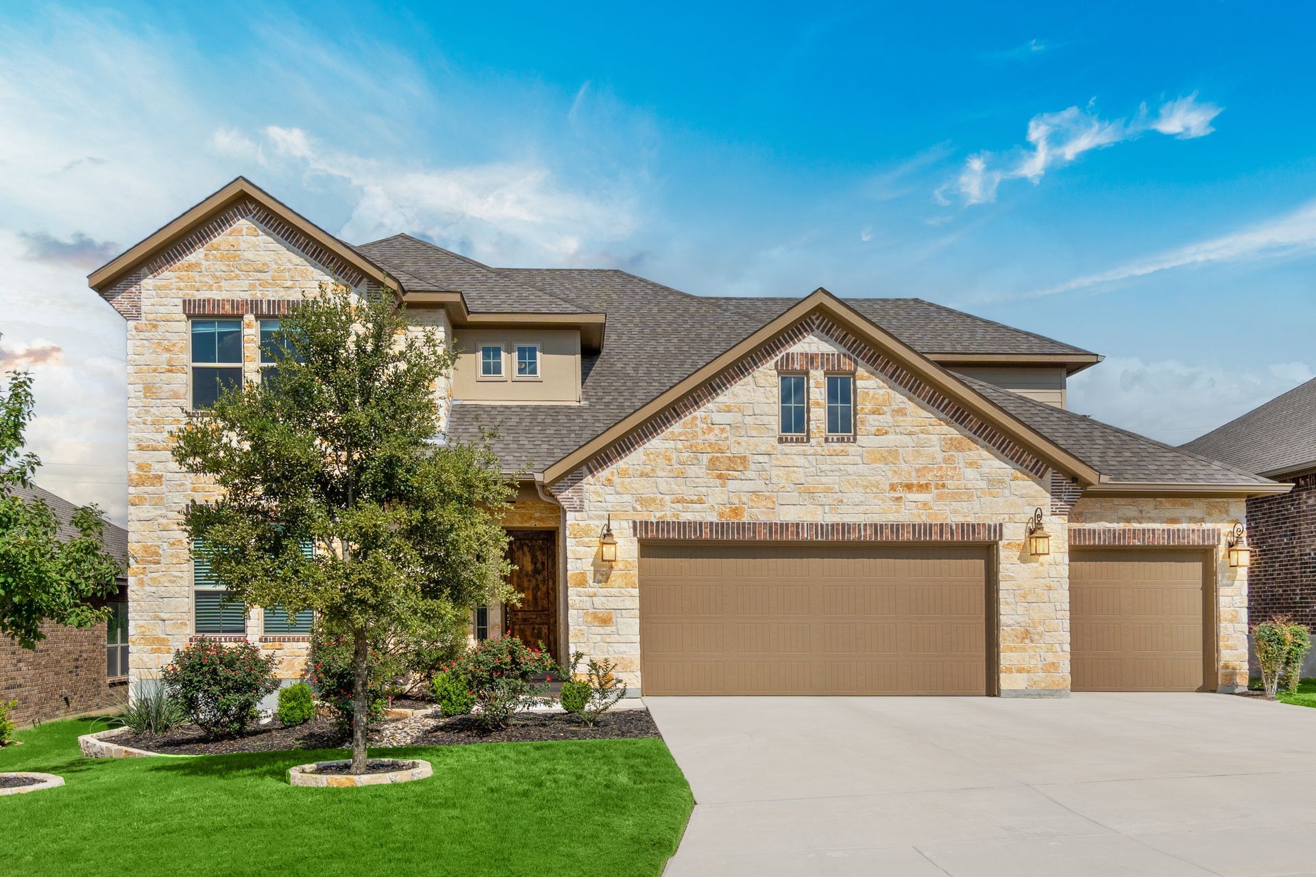 Two-story stone house with brown roof, three-car garage, and landscaped front yard