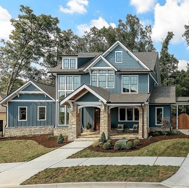 Blue two-story house with stone accents and a porch, set on a green lawn under a cloudy sky.