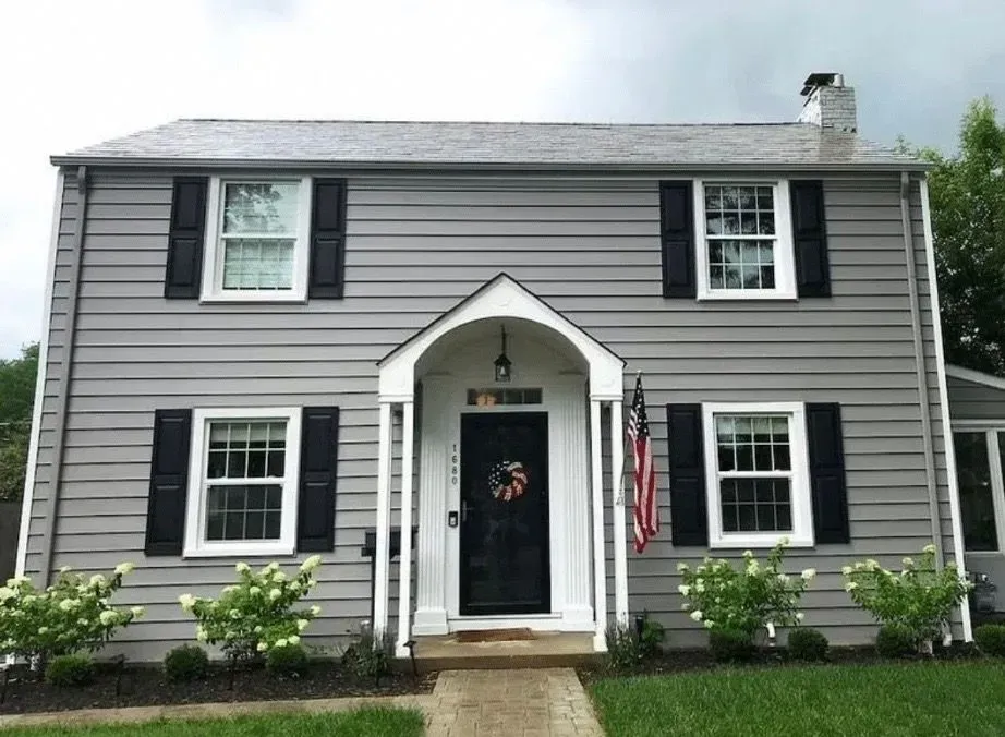 Gray two-story house with black shutters, white trim, and a front porch. An American flag hangs.