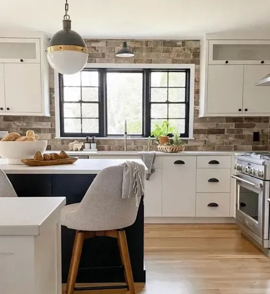 White and black kitchen with brick backsplash, island, window, and wooden floor.