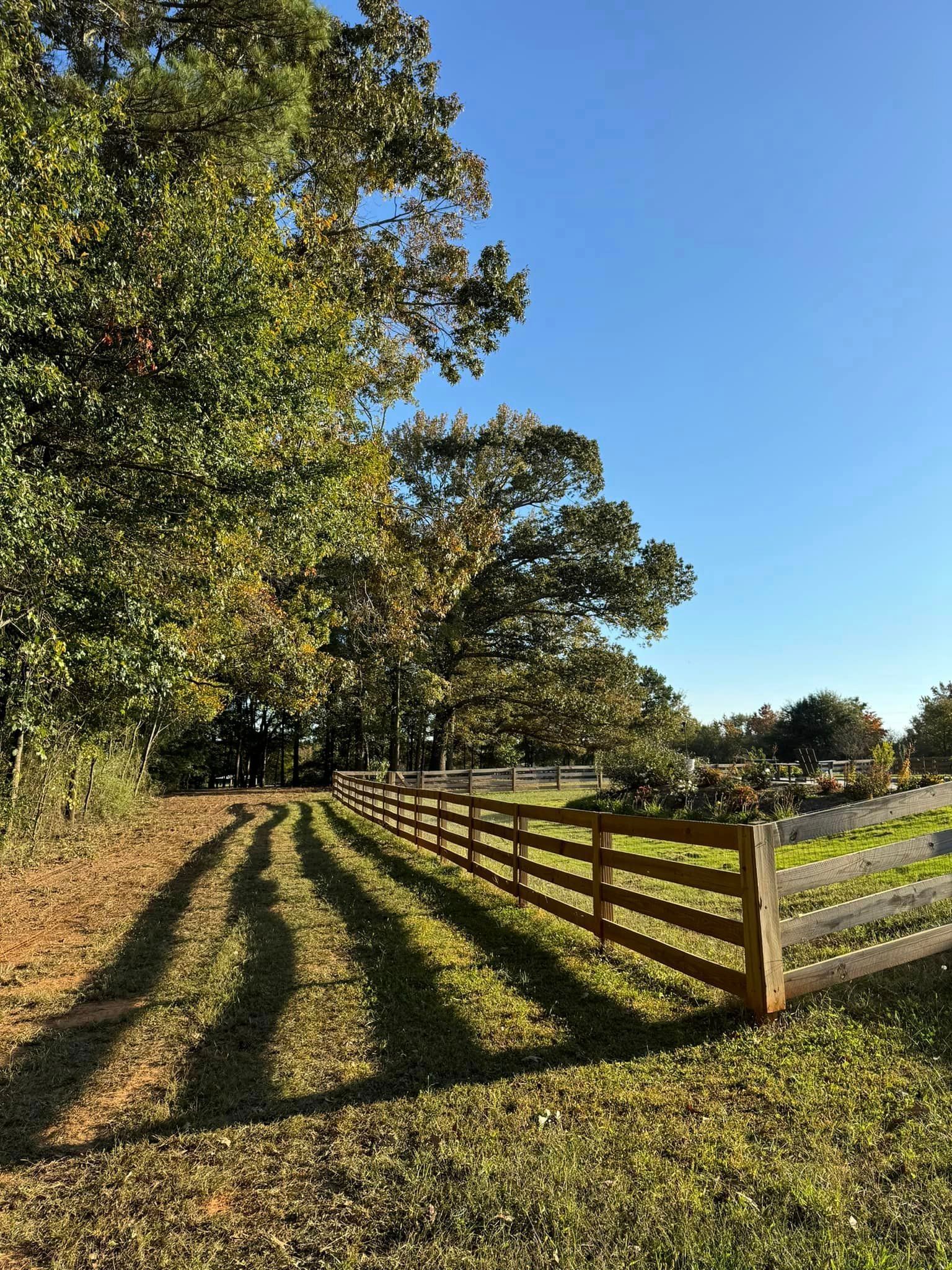 A wooden fence along a dirt road with trees in the background.