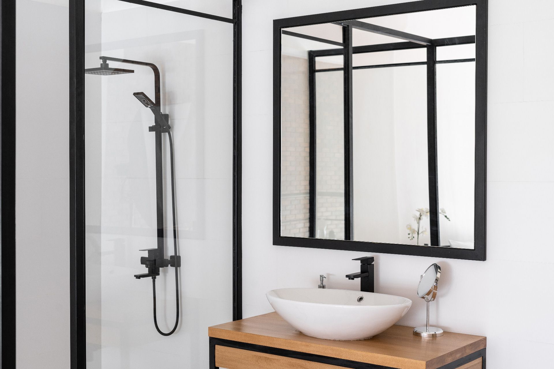 Baño moderno con ducha y espejo con marco negro, lavabo blanco y tocador de madera.