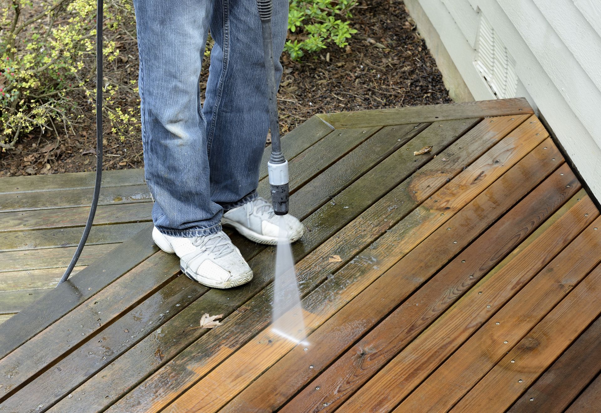 Person using a power washer to clean a wooden deck.