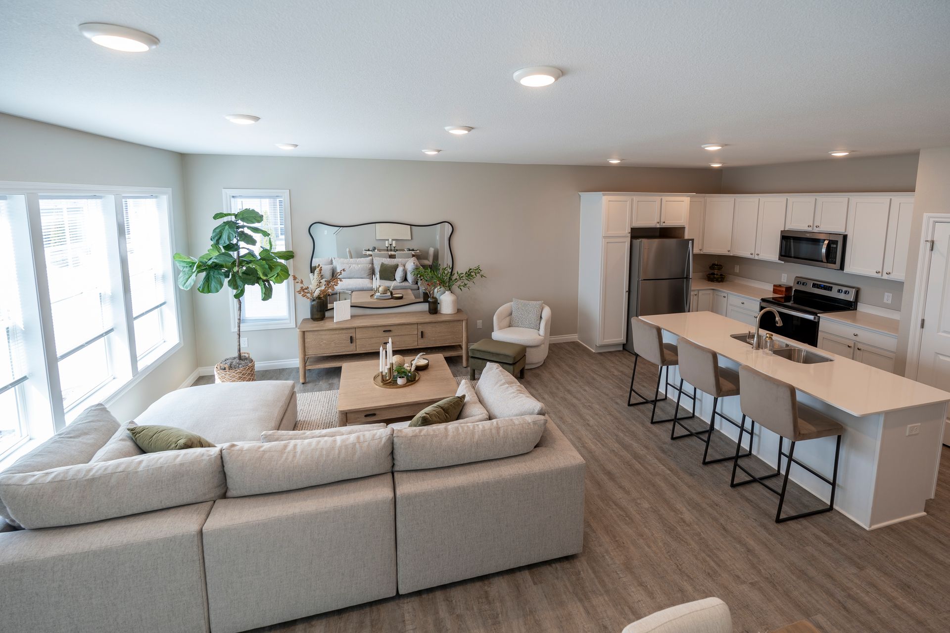 Open-concept living space with kitchen, island with stools, sofa, and large windows. Light color palette.