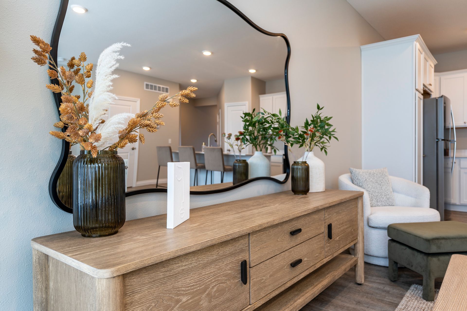 Wooden console table with vases and mirror reflecting a kitchen and living room.