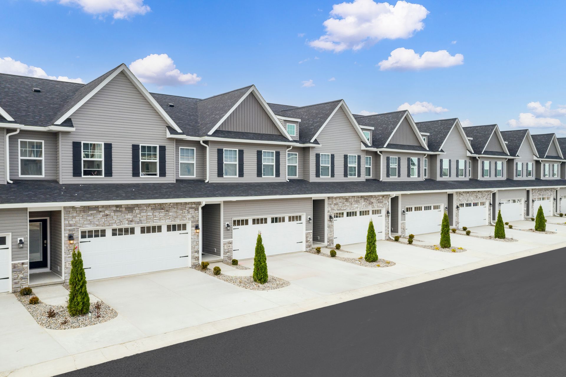 Row of modern townhouses with grey siding, white garage doors, and small trees.