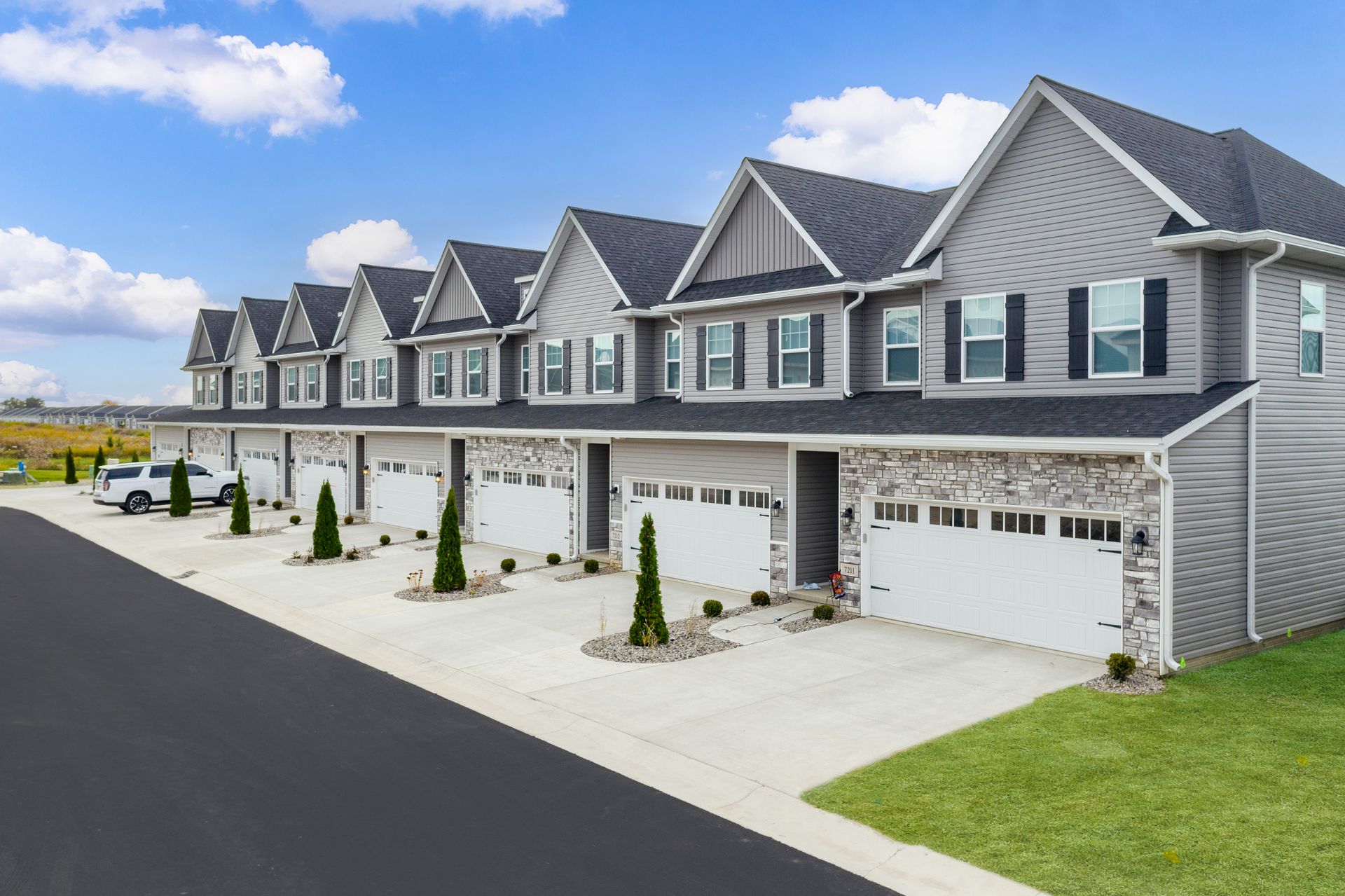 Row of modern townhouses with gray siding, white garages, and black shutters, under a blue sky.