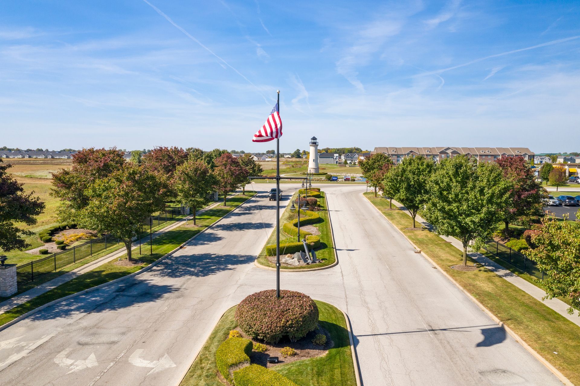 A road lined with trees and landscaping leads to a tall flagpole with an American flag.
