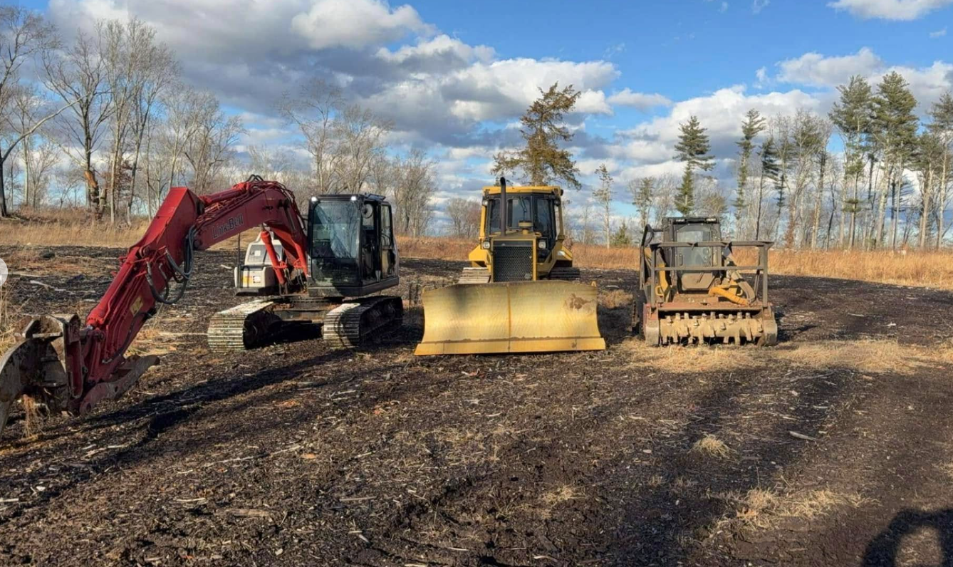 Three pieces of heavy construction equipment on cleared land: excavator, bulldozer, and skid steer.