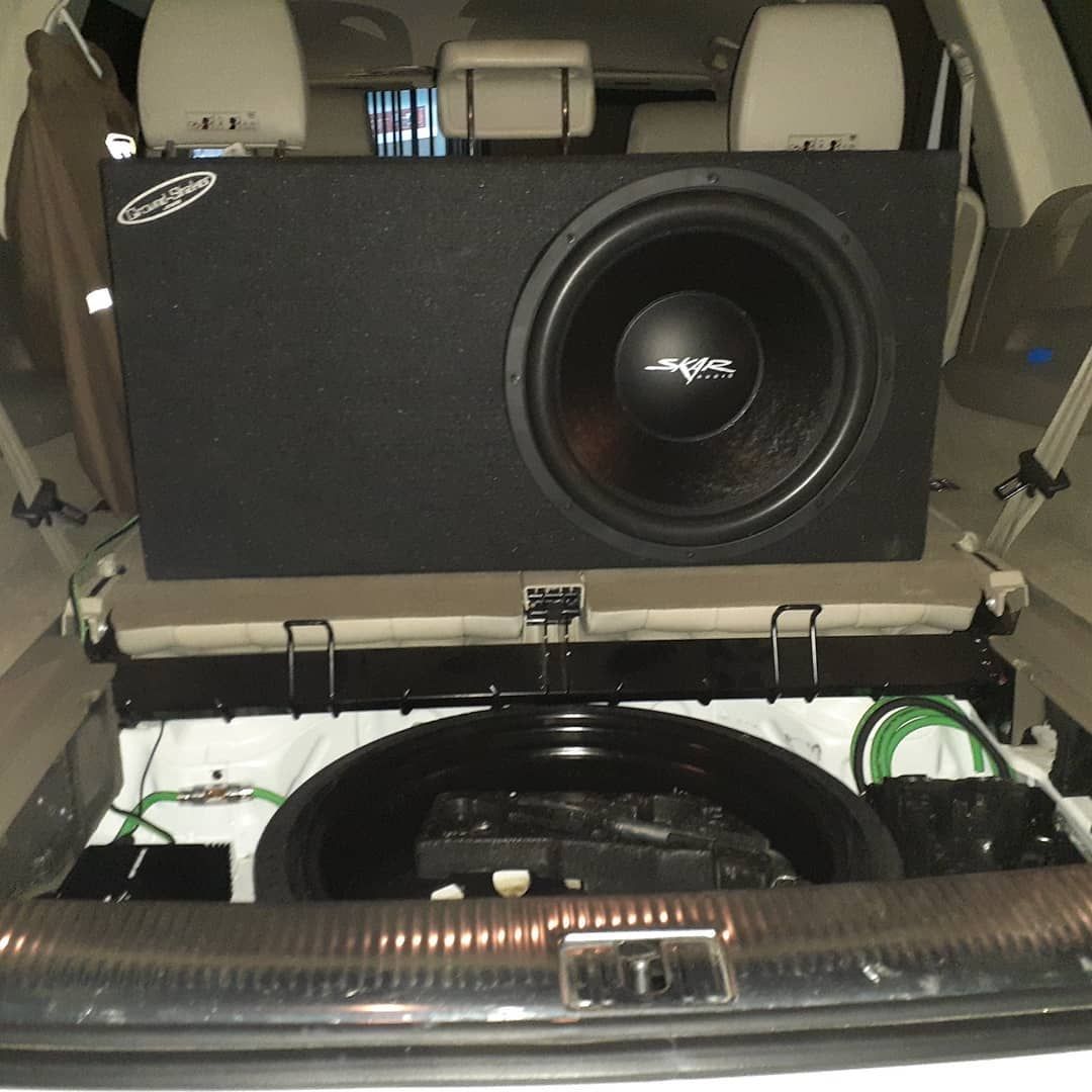 A car trunk with a large black subwoofer box. The spare tire well is visible below the subwoofer.