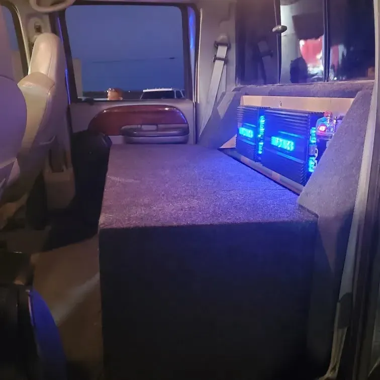 Back of a vehicle customized with audio equipment, including amplifiers with blue lights and a covered enclosure.