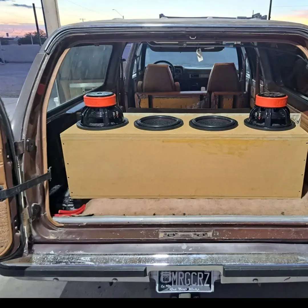 Back of a brown SUV with a large wooden speaker box containing three are mounted on top of the box.