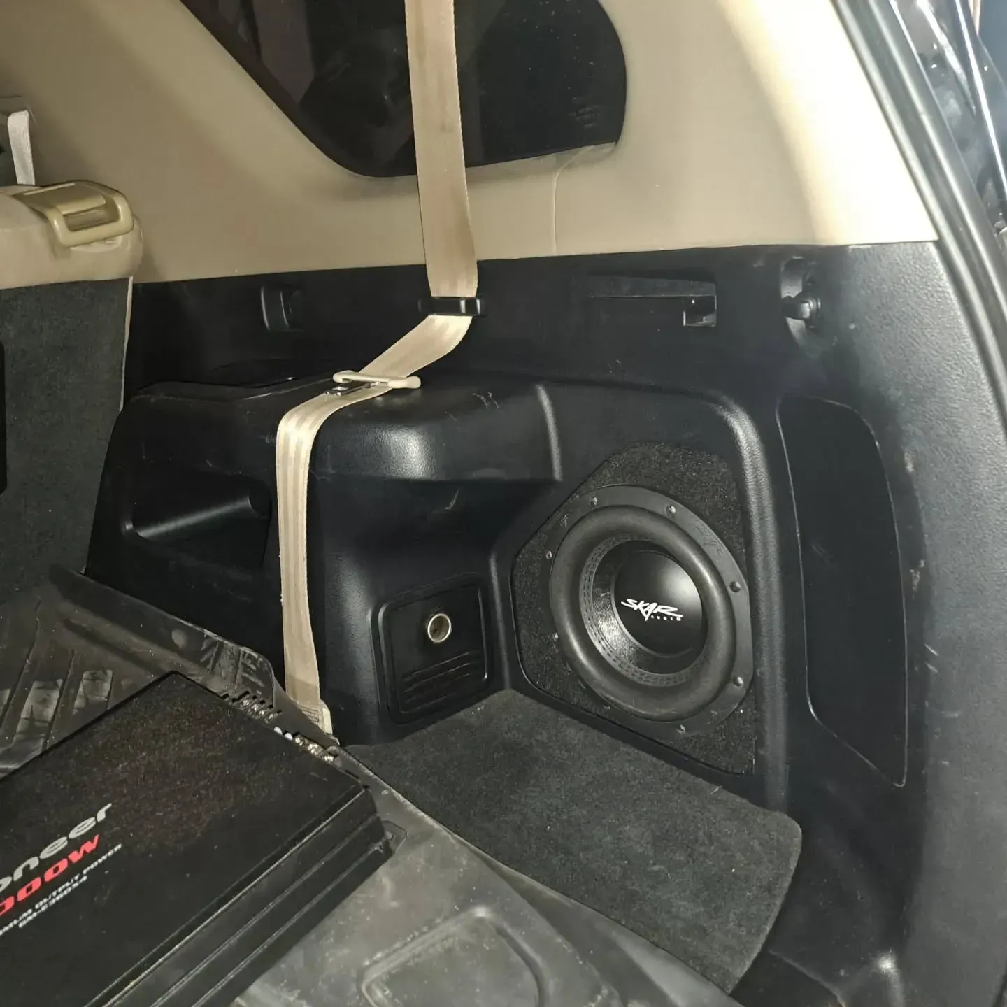 Interior of a car's trunk with a subwoofer and amplifier installed. The subwoofer is in a custom enclosure.