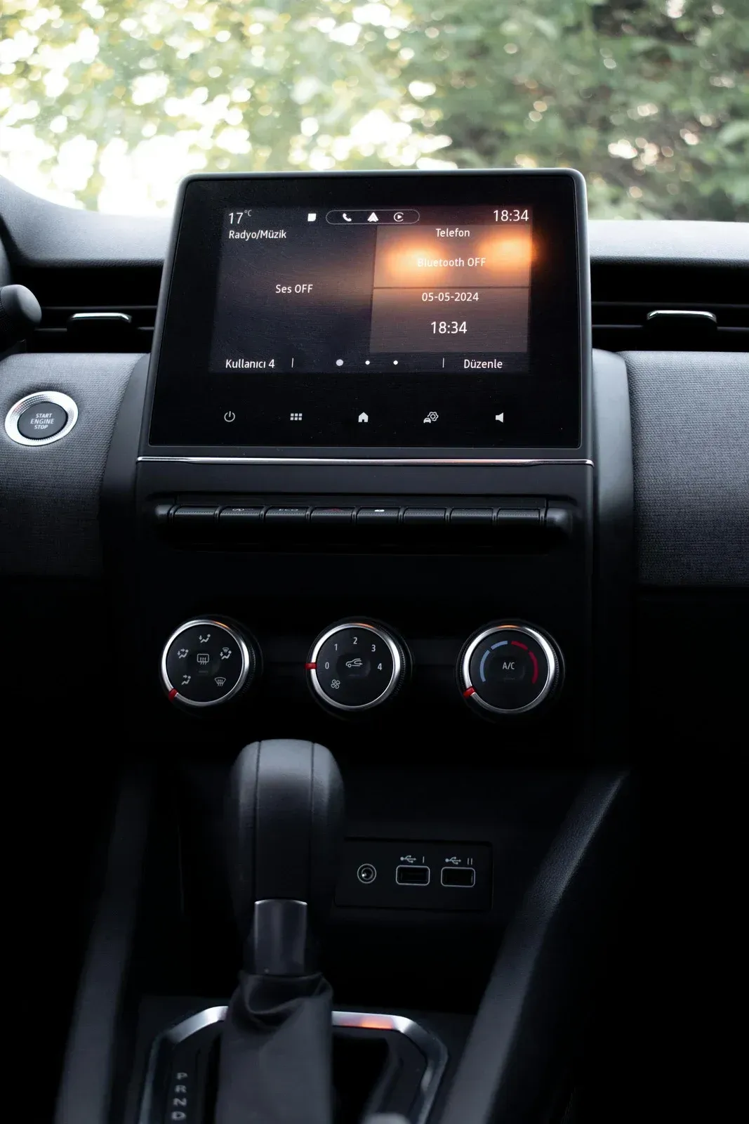 Dashboard of a car featuring a touchscreen display with music information and climate control knobs. The gear shift and c