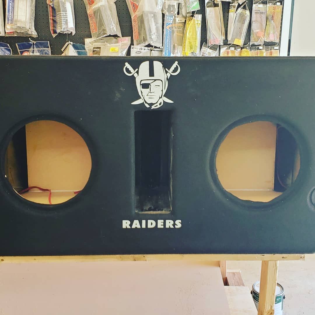 Black Raiders-themed subwoofer box with two speaker holes and a center slot, sitting on a workbench.