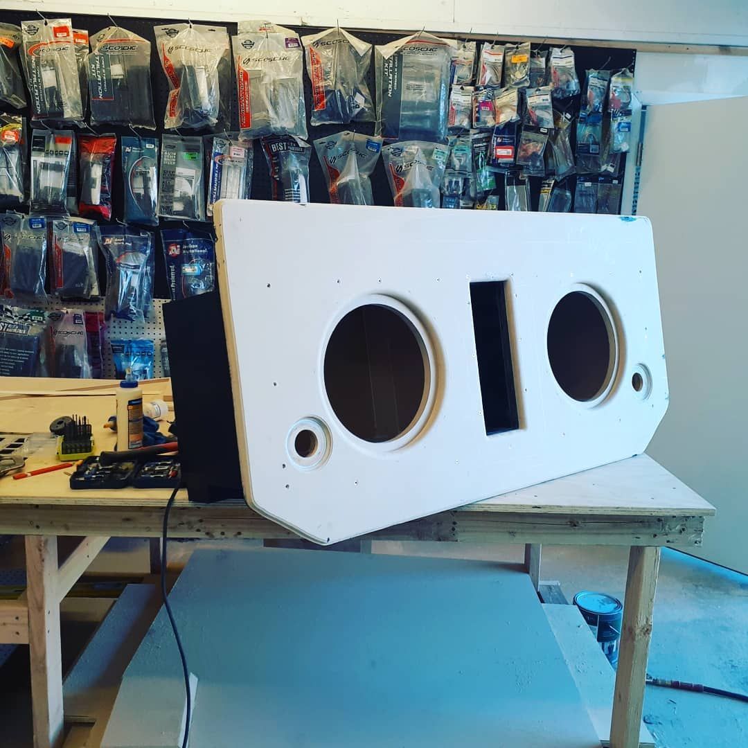 White subwoofer enclosure with speaker cutouts sits on a wooden work table in a 