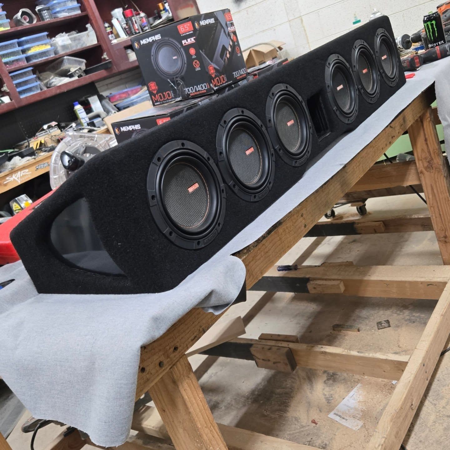Black speaker enclosure with six speakers on a wooden stand in a shop.