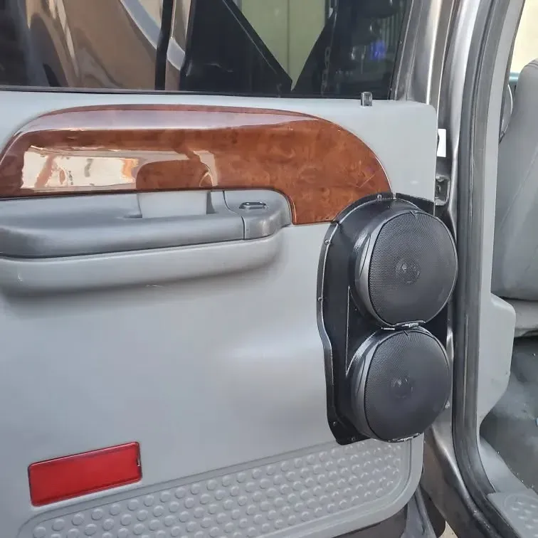 Car door interior with gray paneling and a wood grain accent. Black speakers are mounted on a custom black bracket.