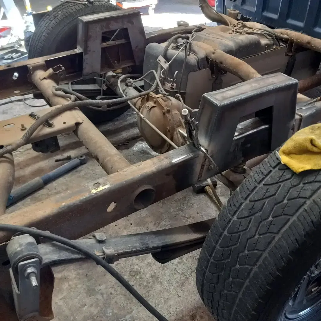 Rusty truck chassis with a tire, exposed engine components, and welding work.