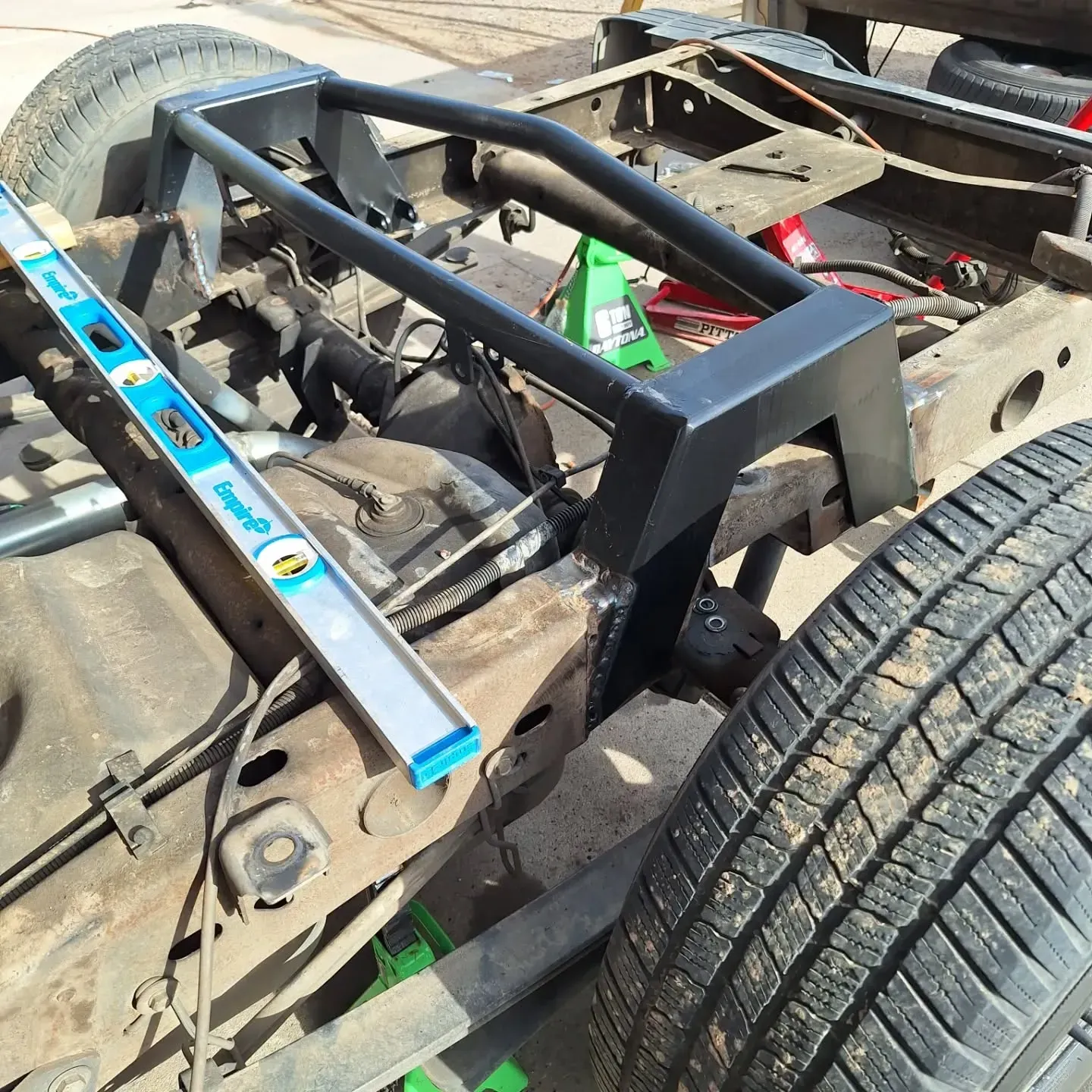 Black metal fabricated frame being installed on the chassis of a truck, with a level resting on the frame.
