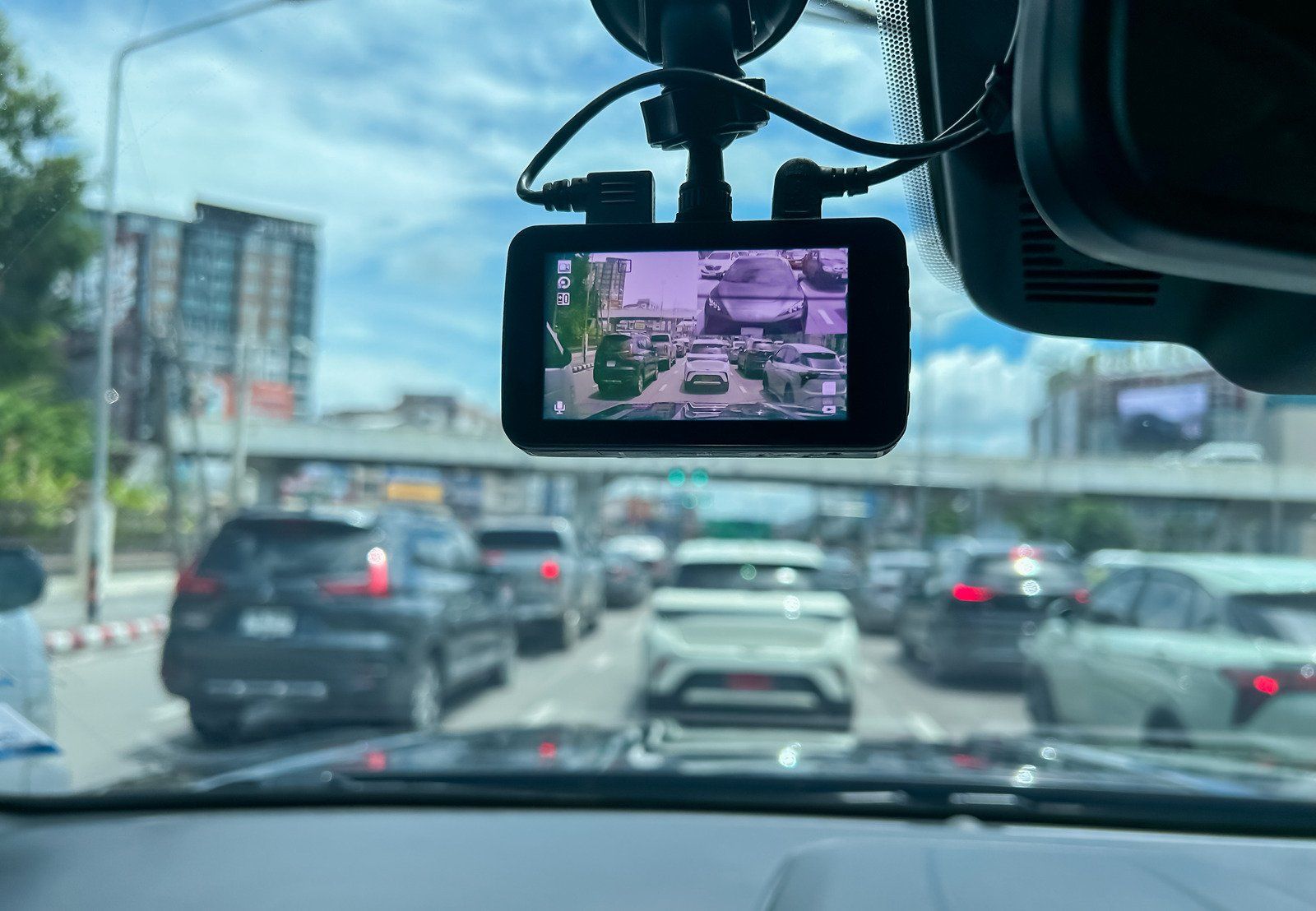 Dashcam view of traffic on a city street, showing cars in a queue on a cloudy day.