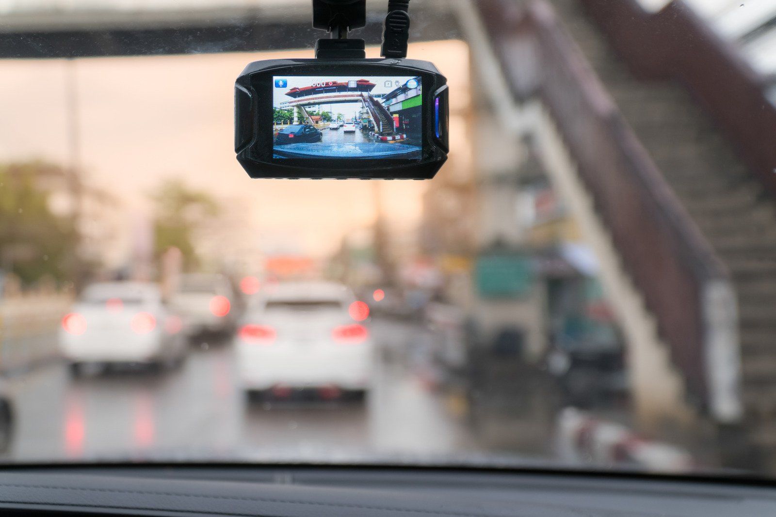 Dashcam recording traffic on a wet road under a bridge, showing other cars in the blurred background.