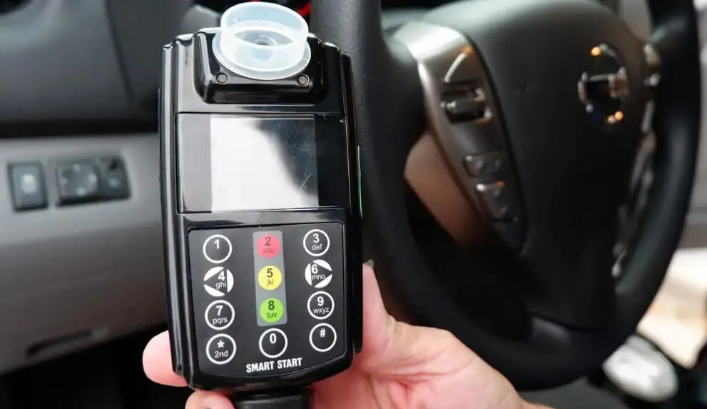 A person holding a black ignition interlock device inside a car, n